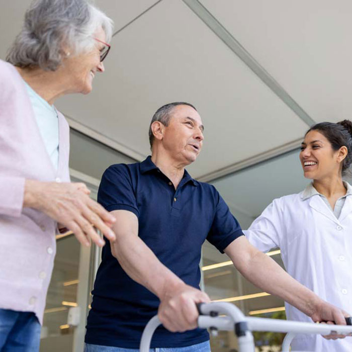 Patient with mobility condition walking with walking frame alongside care worker and visitor.